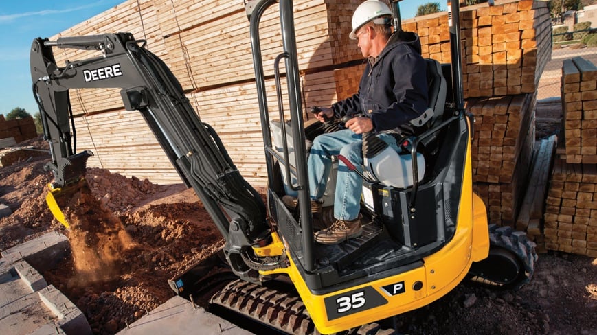John Deere compact excavator being used on a tight jobsite to fill in dirt