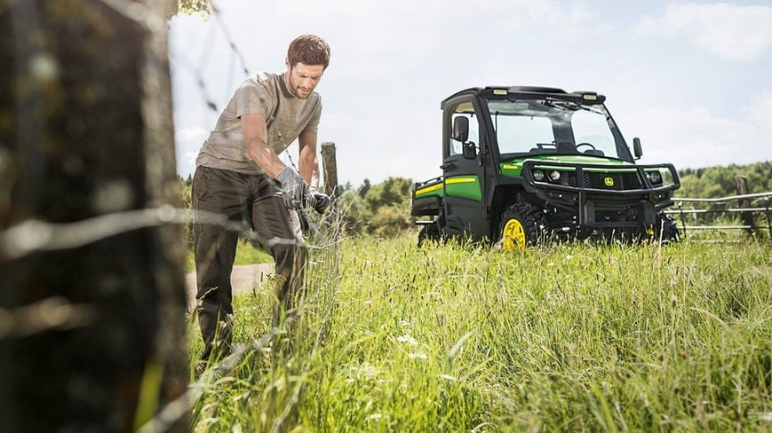 Man with John Deere XUV Gator in the background fixing livestock fencing